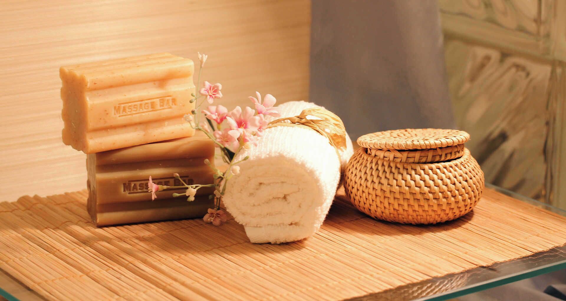 A stack of massage bars, a rolled towel, and a woven basket on a wooden surface.