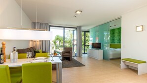 A modern living room with a dining area, a sofa, a TV, and a balcony with a view. - Carat Residenz-Apartmenthaus (Groemitz)