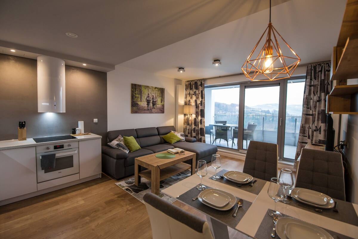 A modern living room with a dining area, a kitchen, and a large window with a city view.