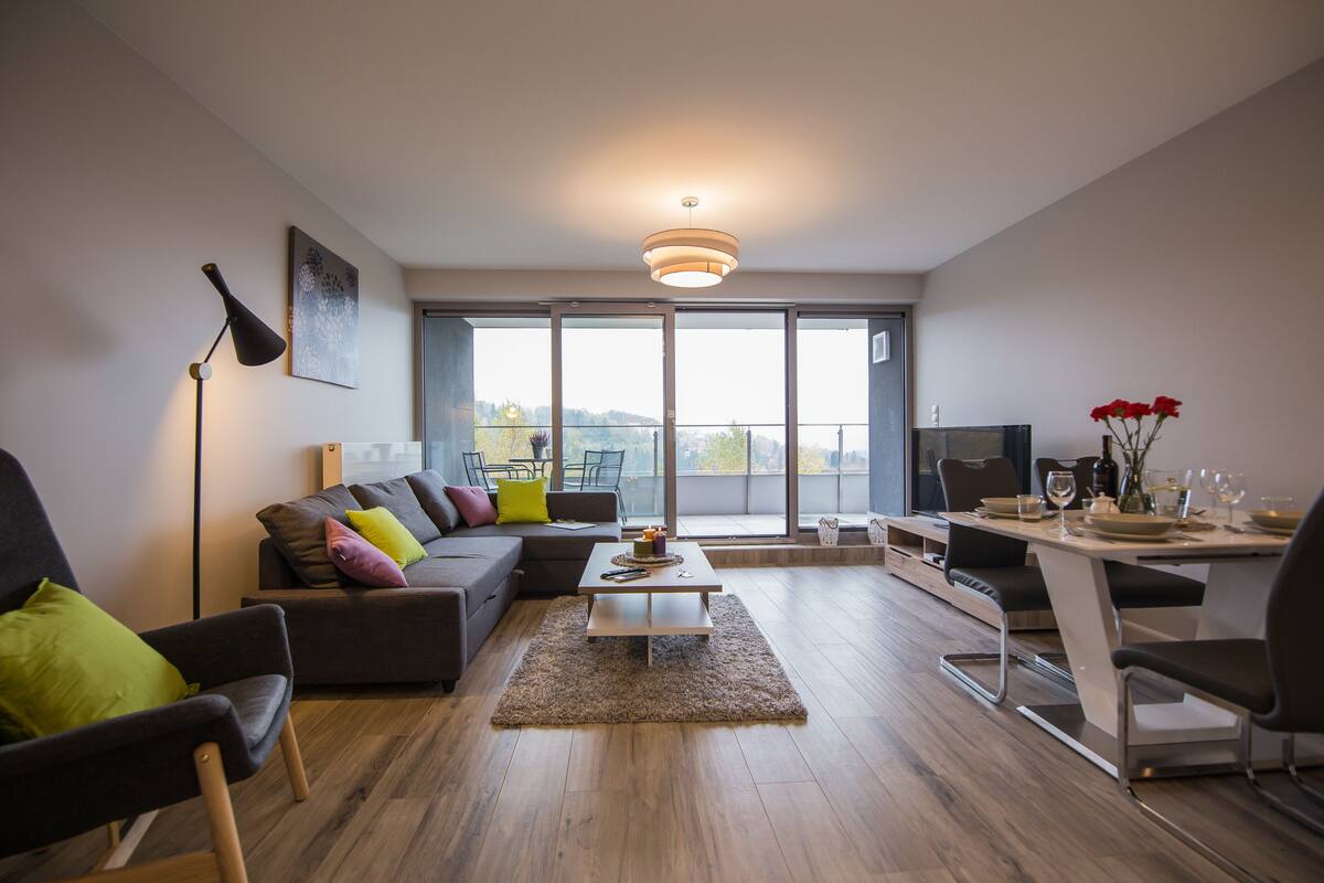 A modern living room with a sectional sofa, a coffee table, and a dining area with chairs and a table set for a meal.