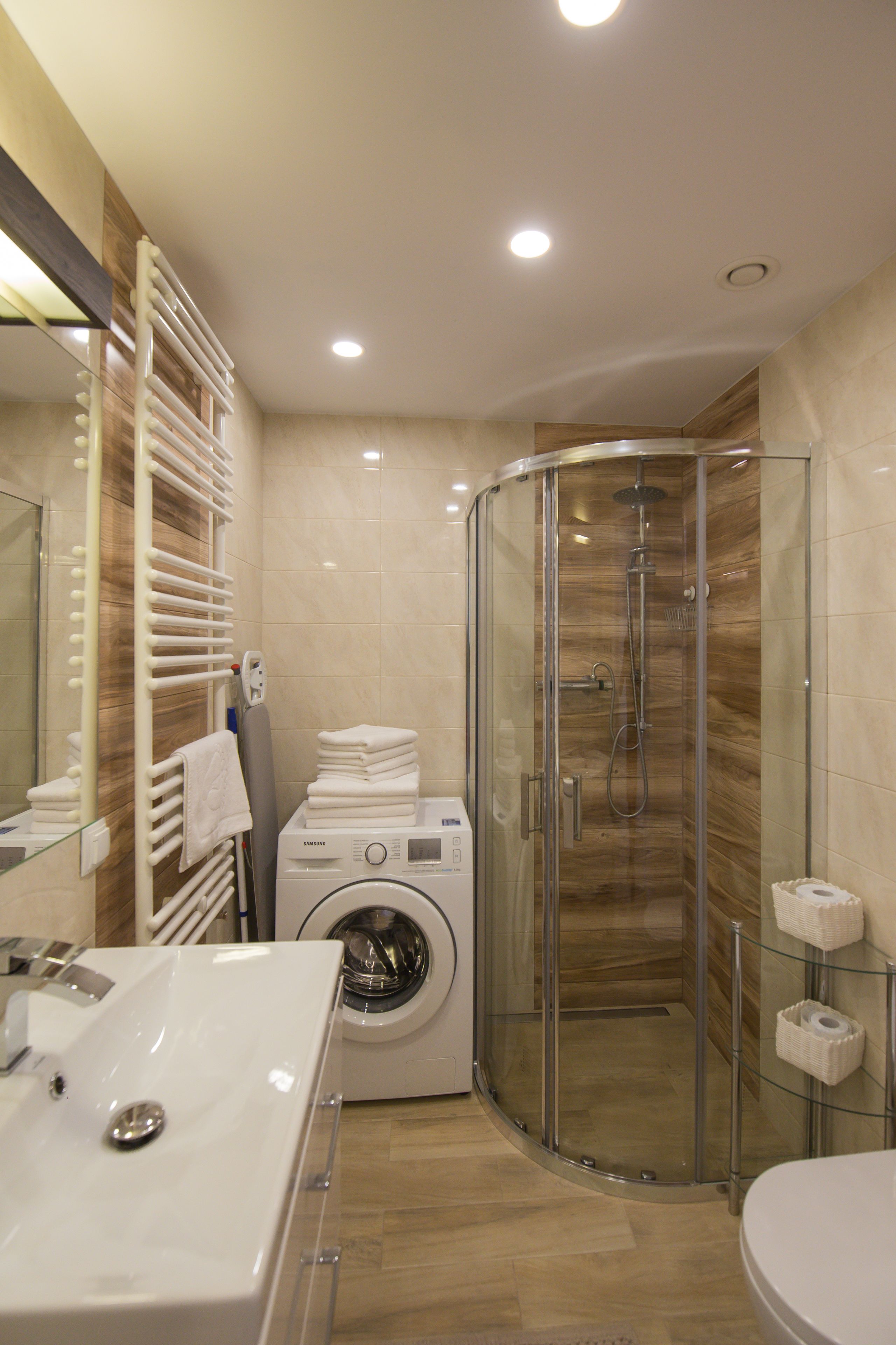 A modern bathroom with a glass shower enclosure, a built-in washing machine, and a large mirror.