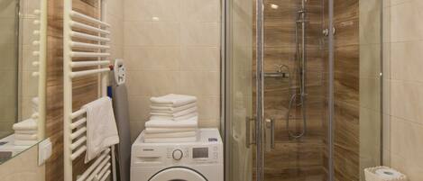 A modern bathroom with a glass shower enclosure, a built-in washing machine, and a large mirror.
