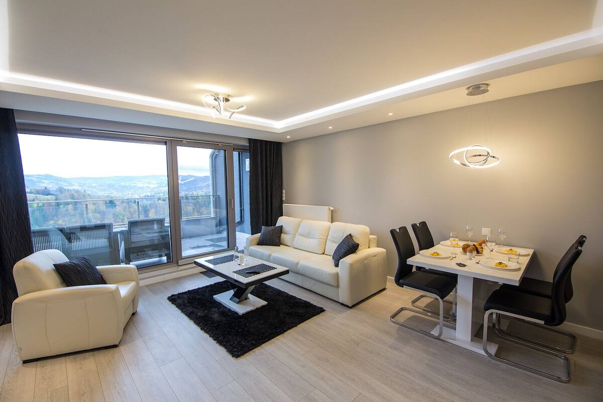 A modern living room with a sofa, a coffee table, and a dining area with chairs and a table set for two.