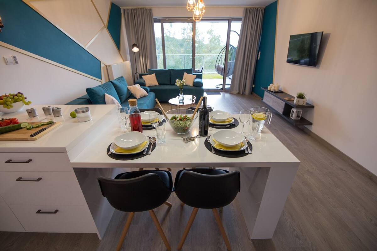 A modern kitchen with a dining area, a sofa, and a TV.