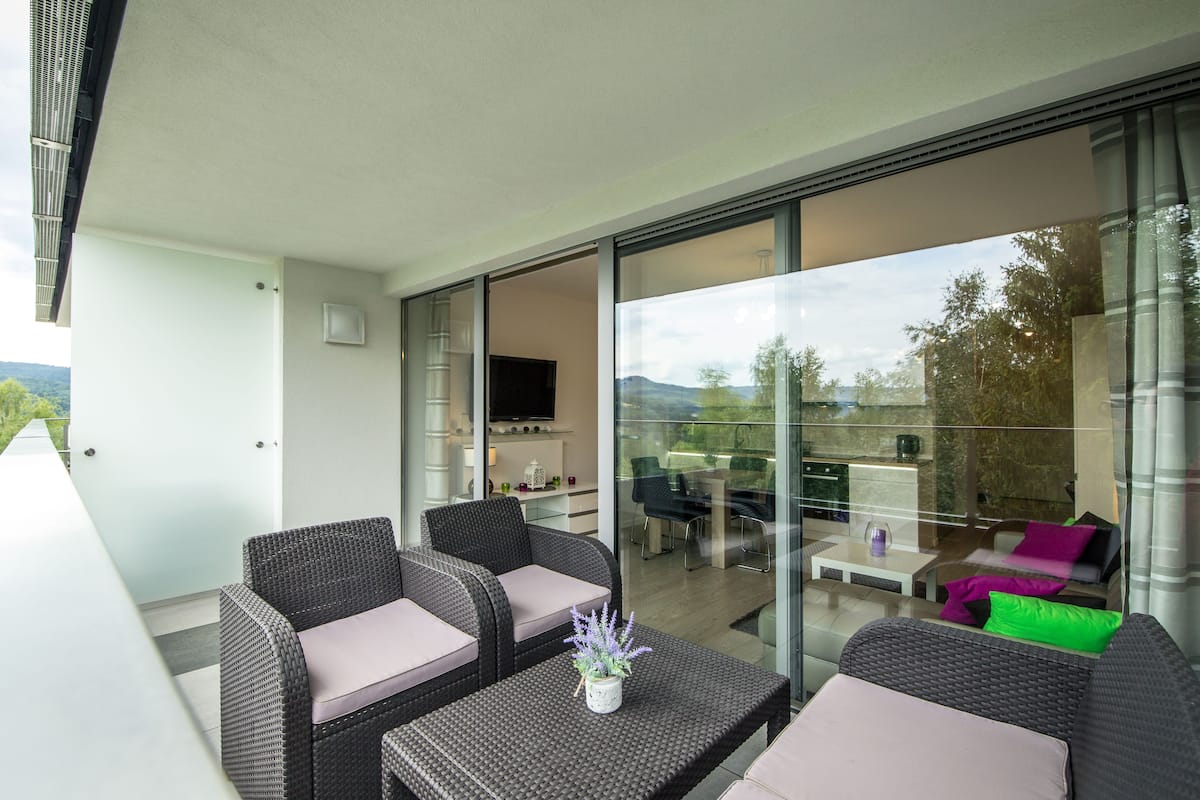 A modern outdoor living area with wicker furniture, a flat-screen TV, and a glass door leading to a dining area.