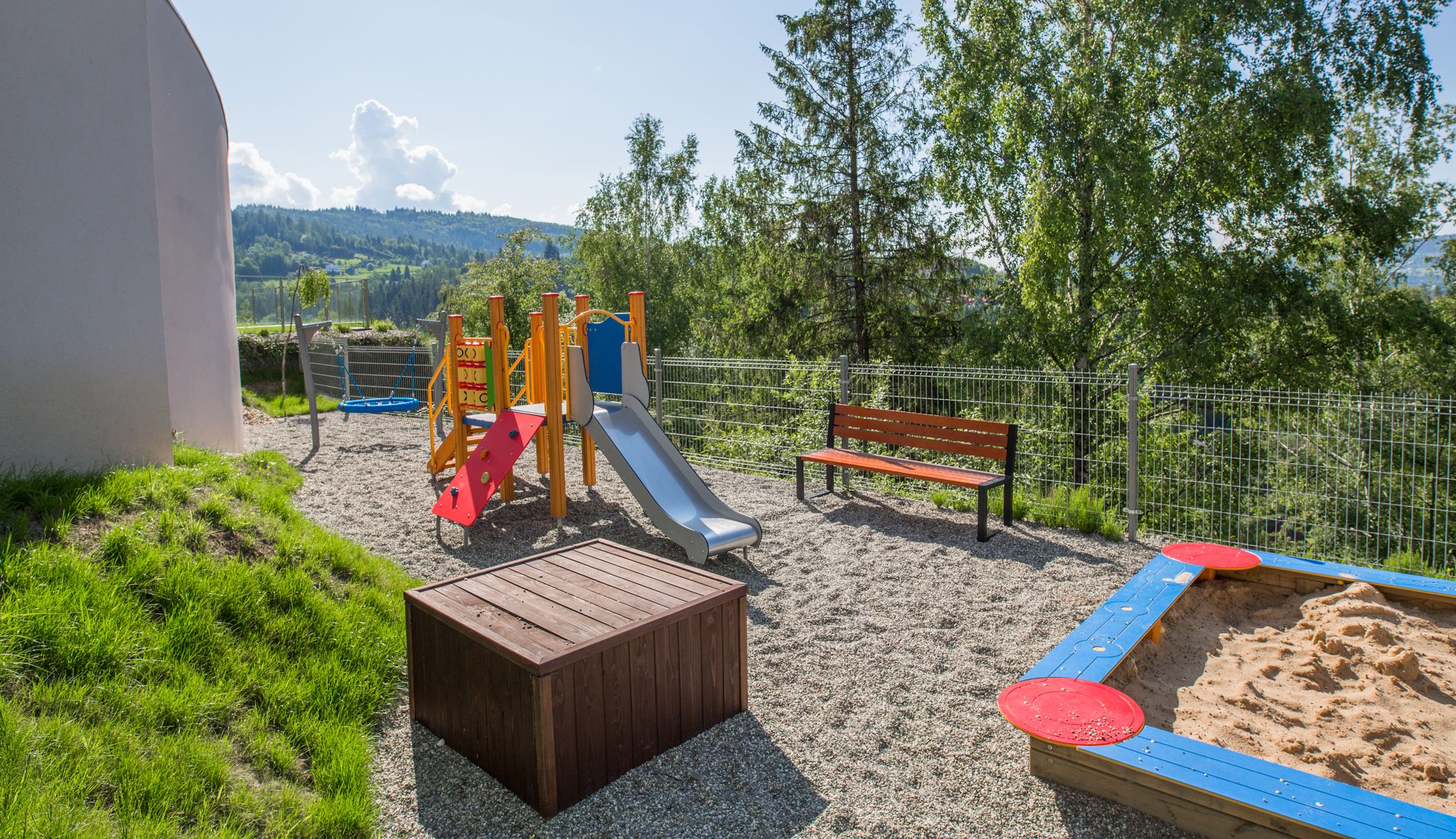 A playground with a slide, a bench, and a sandpit.