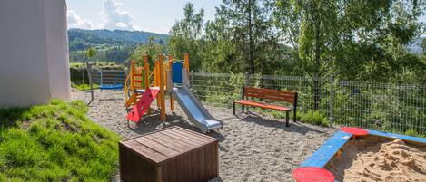 A playground with a slide, a bench, and a sandpit.