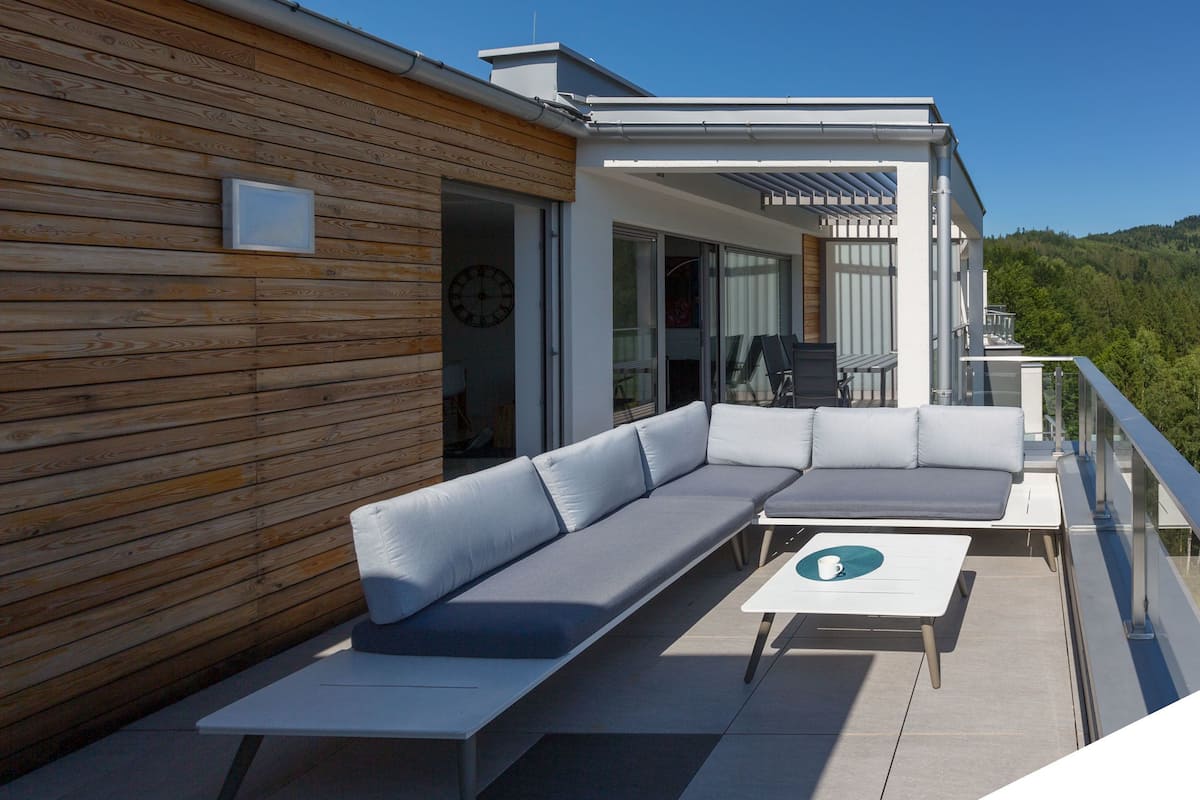 A modern outdoor seating area with a wooden wall, a sofa, and a table.