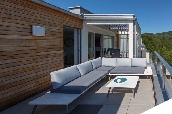 A modern outdoor seating area with a wooden wall, a sofa, and a table.