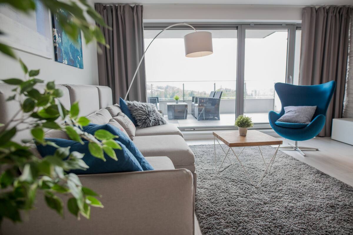 A modern living room with a sofa, a blue chair, a coffee table, and a view through a glass door to an outdoor balcony.