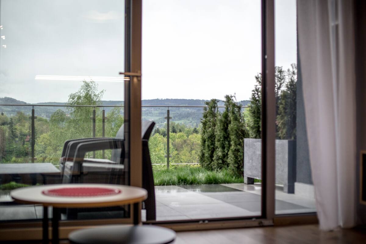 A modern room with a large sliding glass door leading to a balcony with a scenic view of greenery and hills.