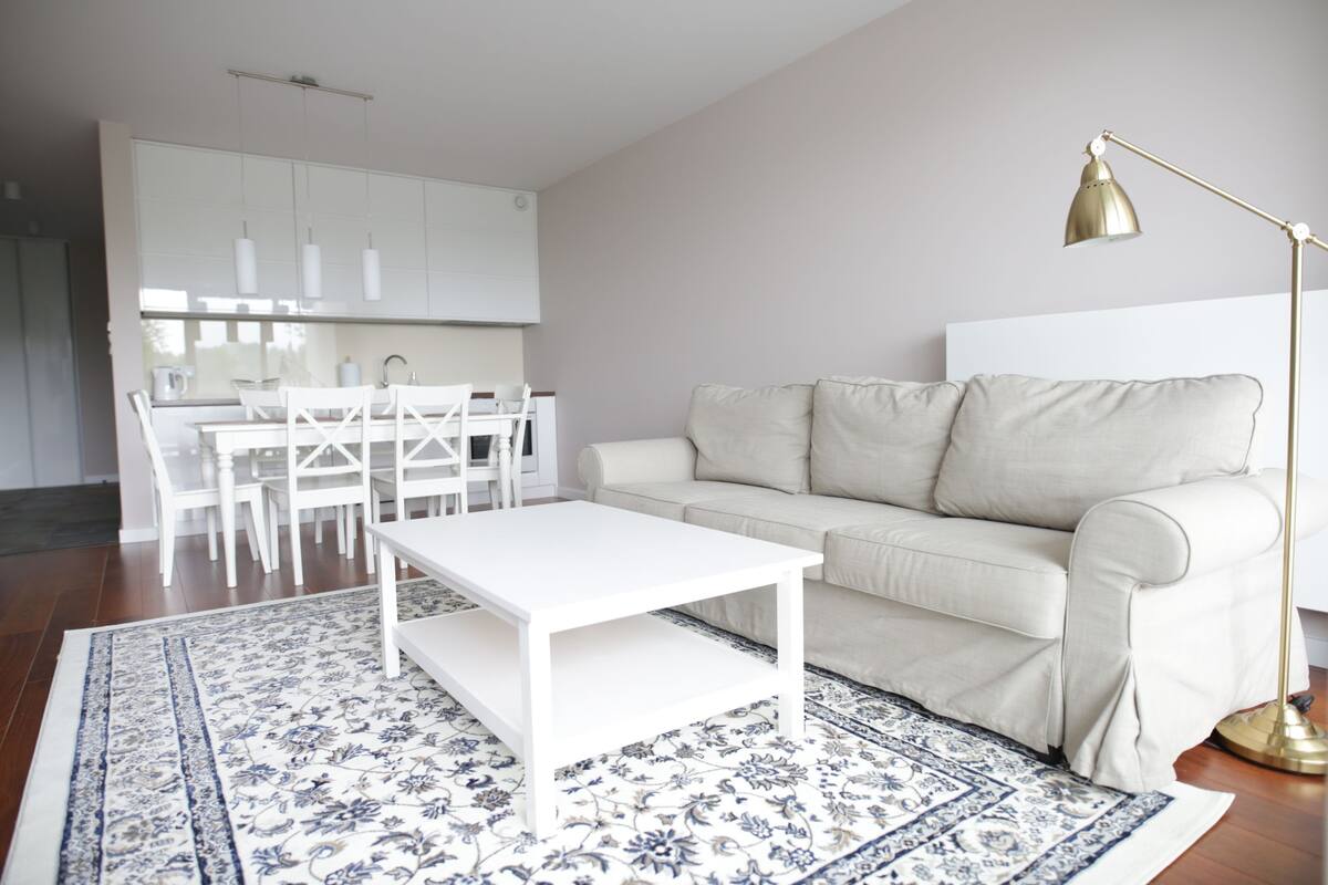 A modern living room with a white sofa, a white coffee table, and a patterned rug.