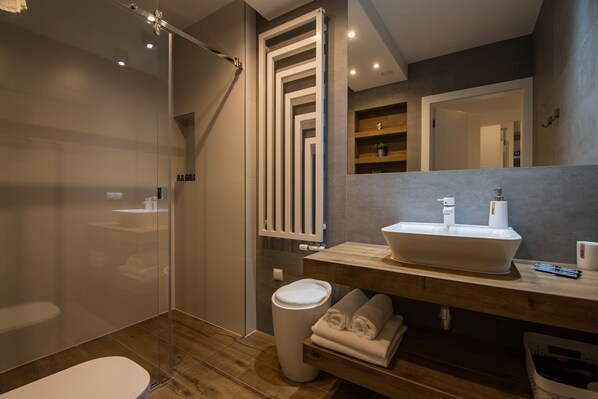 A modern bathroom with a glass shower enclosure, a wooden vanity with a white sink, and a mirror above the sink.