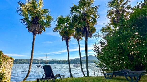 A beach with palm trees, a chair, and a table by the water. - 2 bedroom awesome home in Orta San Giulio NO (Orta San Giulio NO)