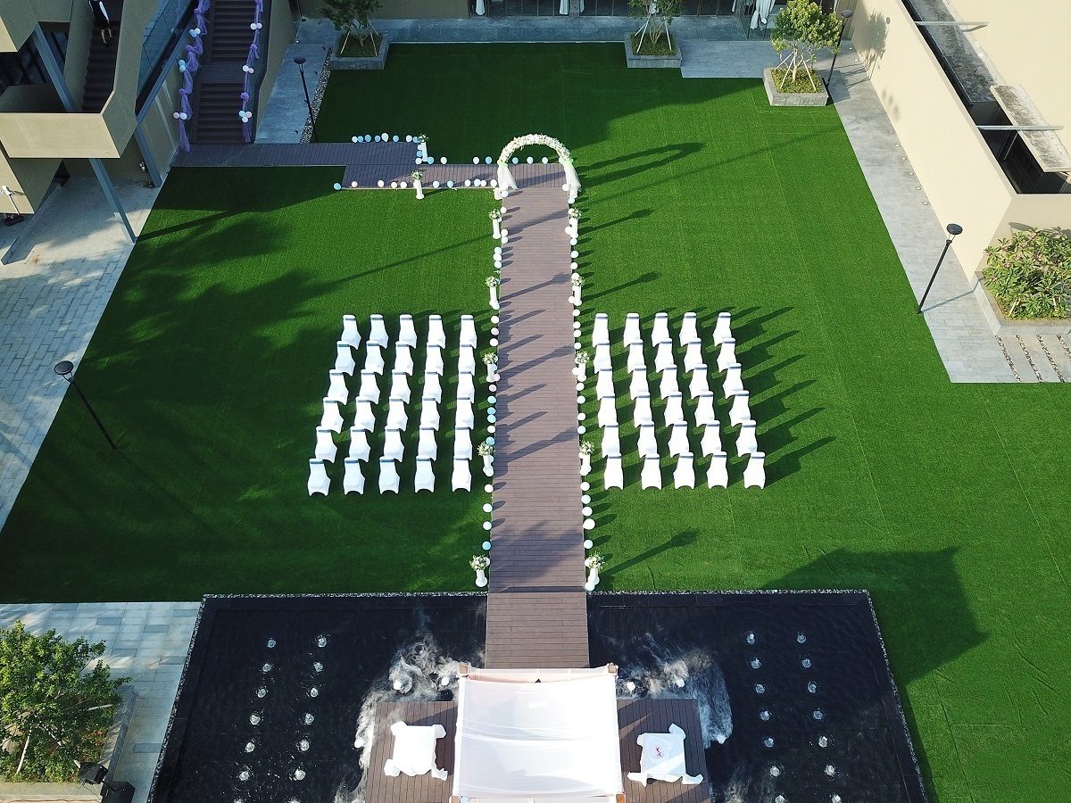An aerial view of a courtyard with a central pathway, surrounded by rows of white chairs and tables, indicating a formal outdoor seating area.