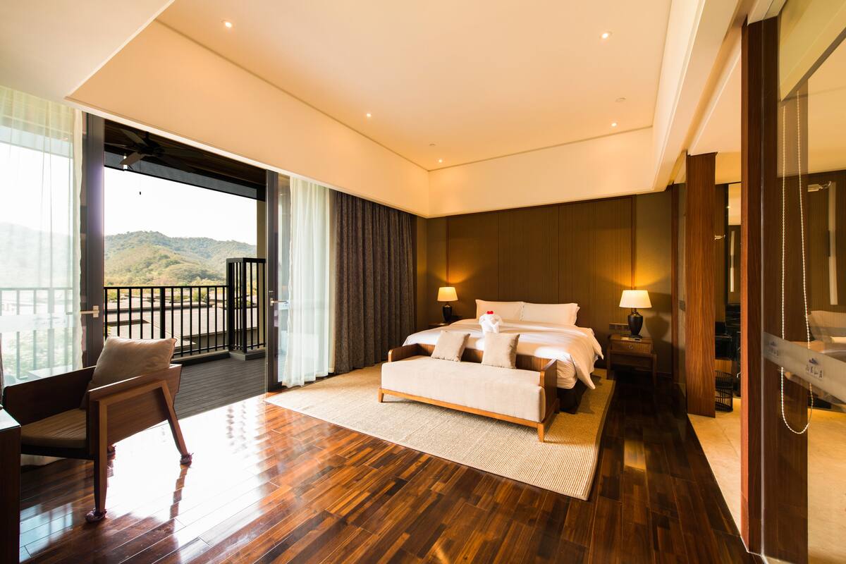 Quarto espaçoso com uma cama grande, área de estar e varanda com vista para as colinas.