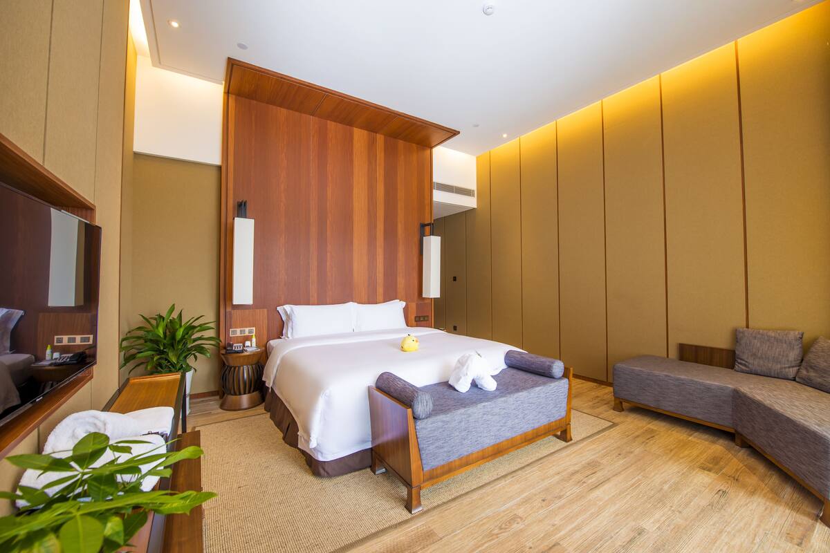 Quarto de hotel moderno com uma cama grande, um sofá, uma escrivaninha com um computador e uma planta em vaso.
