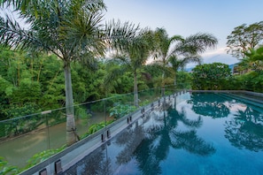 A swimming pool with a glass railing, surrounded by lush greenery and palm trees. - Nankun Shanju Hot Spring Resort (Huizhou)