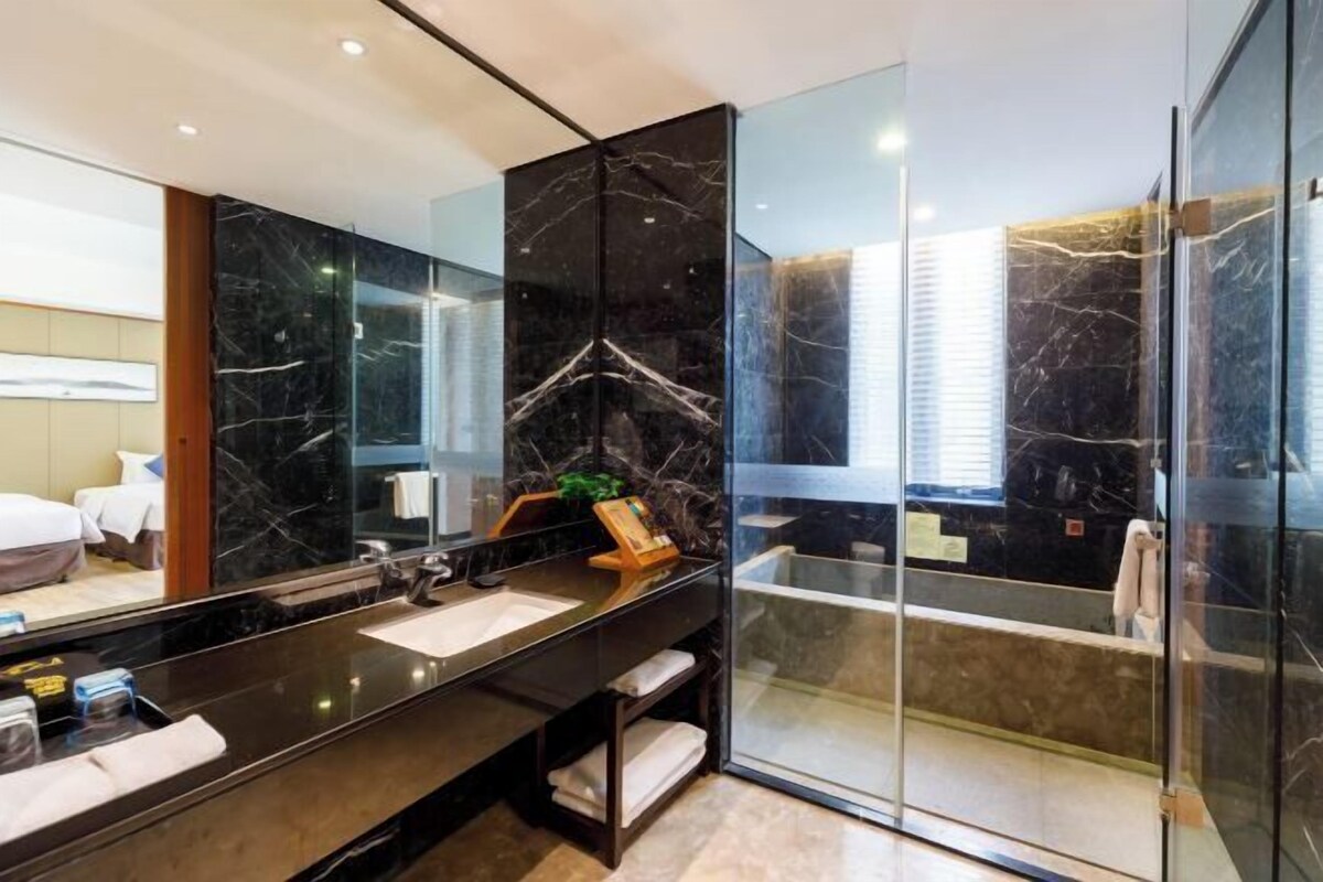 A modern bathroom with a black marble vanity, a glass shower enclosure, and a large mirror reflecting the room.