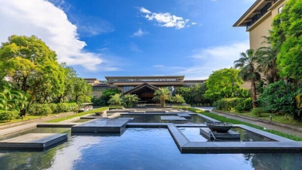 A hotel with a modern architectural design, featuring a central water feature and lush greenery.