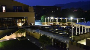 A rooftop pool area with lounge chairs and umbrellas, surrounded by modern buildings and a mountain backdrop.