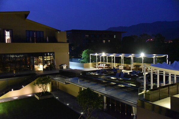 A rooftop pool area with lounge chairs and umbrellas, surrounded by modern buildings and a mountain backdrop. - Nankun Shanju Hot Spring Resort (Huizhou)