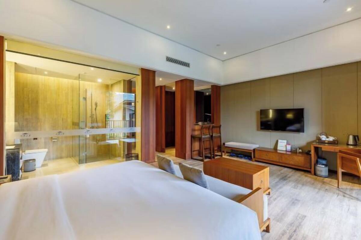 Quarto de hotel moderno com uma cama grande, uma escrivaninha, uma TV e área de chuveiro com divisória de vidro.