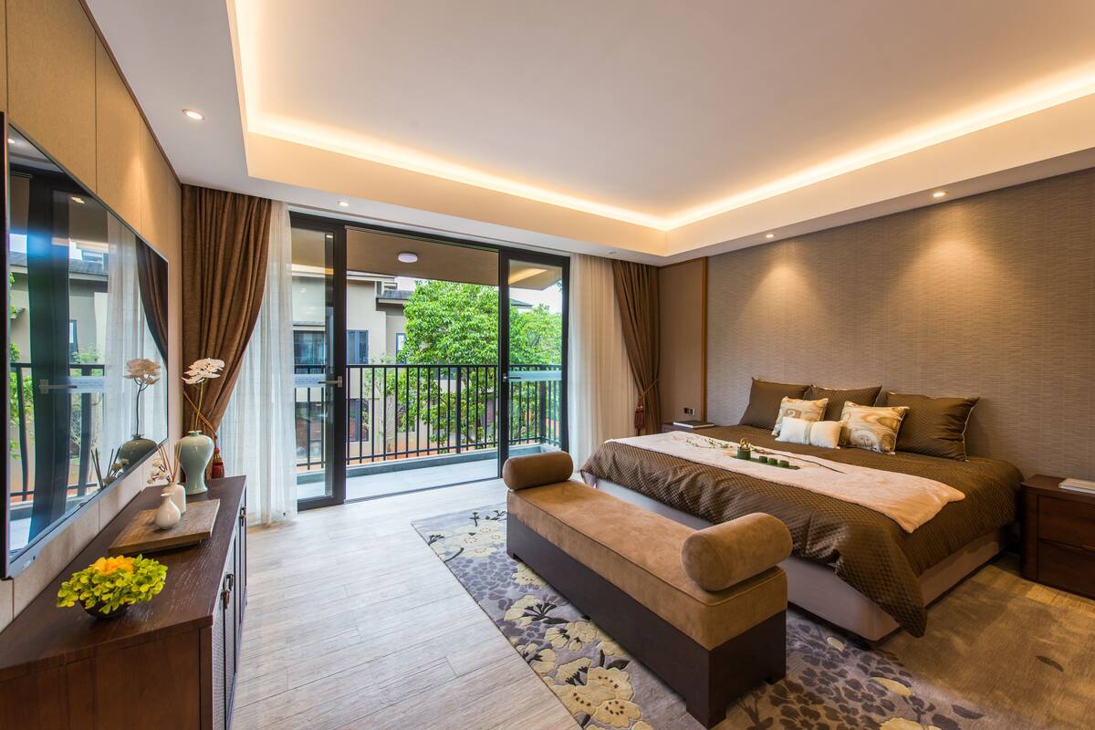 Quarto moderno com cama grande, um banquinho, escrivaninha e vista para uma varanda.