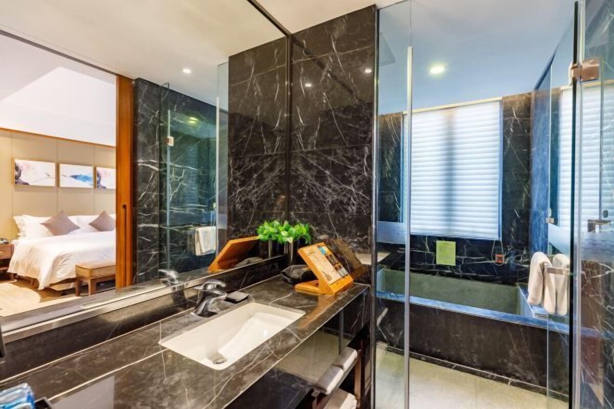 A modern bathroom with a large mirror, a black marble sink, and a bathtub.