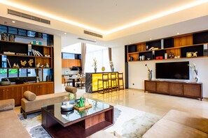 A modern living room with a sofa, coffee table, and entertainment unit. There is a dining area with a table and chairs in the background. - Nankun Shanju Hot Spring Resort (Huizhou)