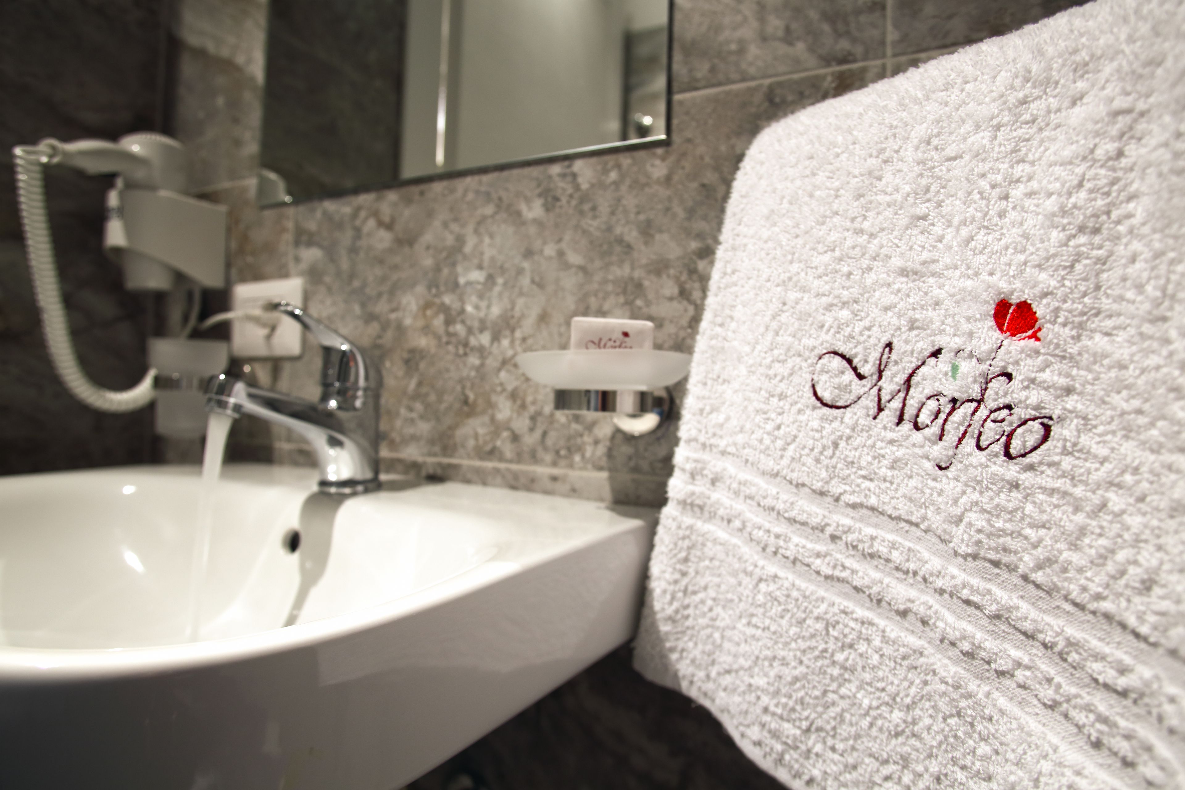 A bathroom with a white sink, a mirror, and a towel with embroidered text.