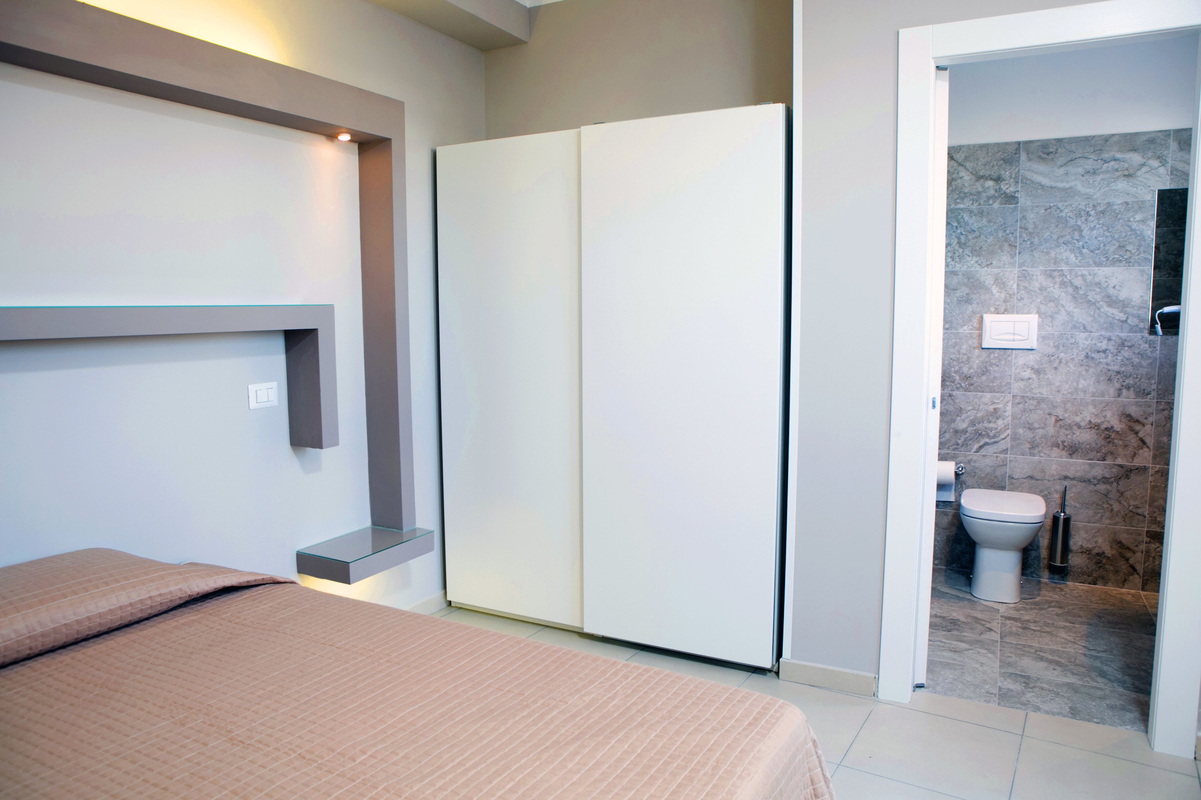 A bedroom with a bed, a wardrobe, and a bathroom with a toilet and shower.