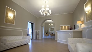 A spacious living room with two white sofas, a chandelier, and a dining area with a table and chairs. - Morfeo Luxury Rooms (Pozzallo)