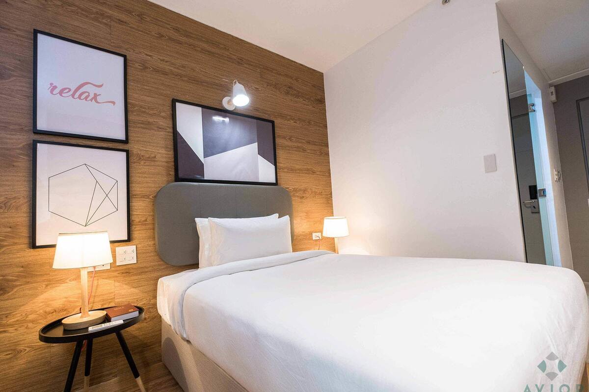 A hotel room with a bed, two wall-mounted lamps, a framed geometric artwork, and a framed word "relax".