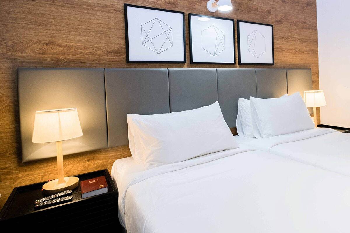 A hotel room with a wooden headboard, a bed with white linens, two bedside lamps, and three framed geometric wall art pieces.