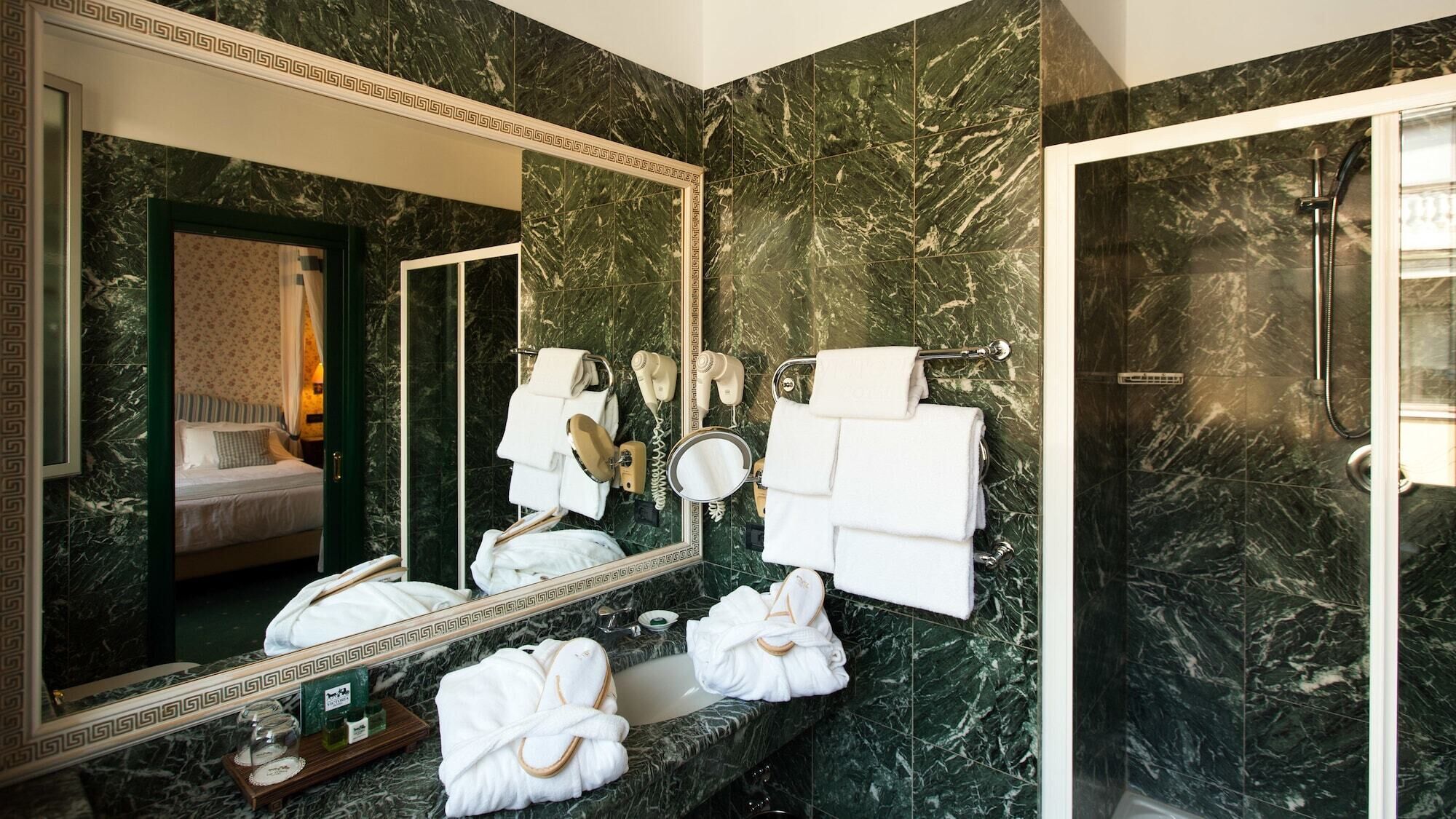 Un baño con un espejo grande, paredes de mármol, ducha y varios toallas.