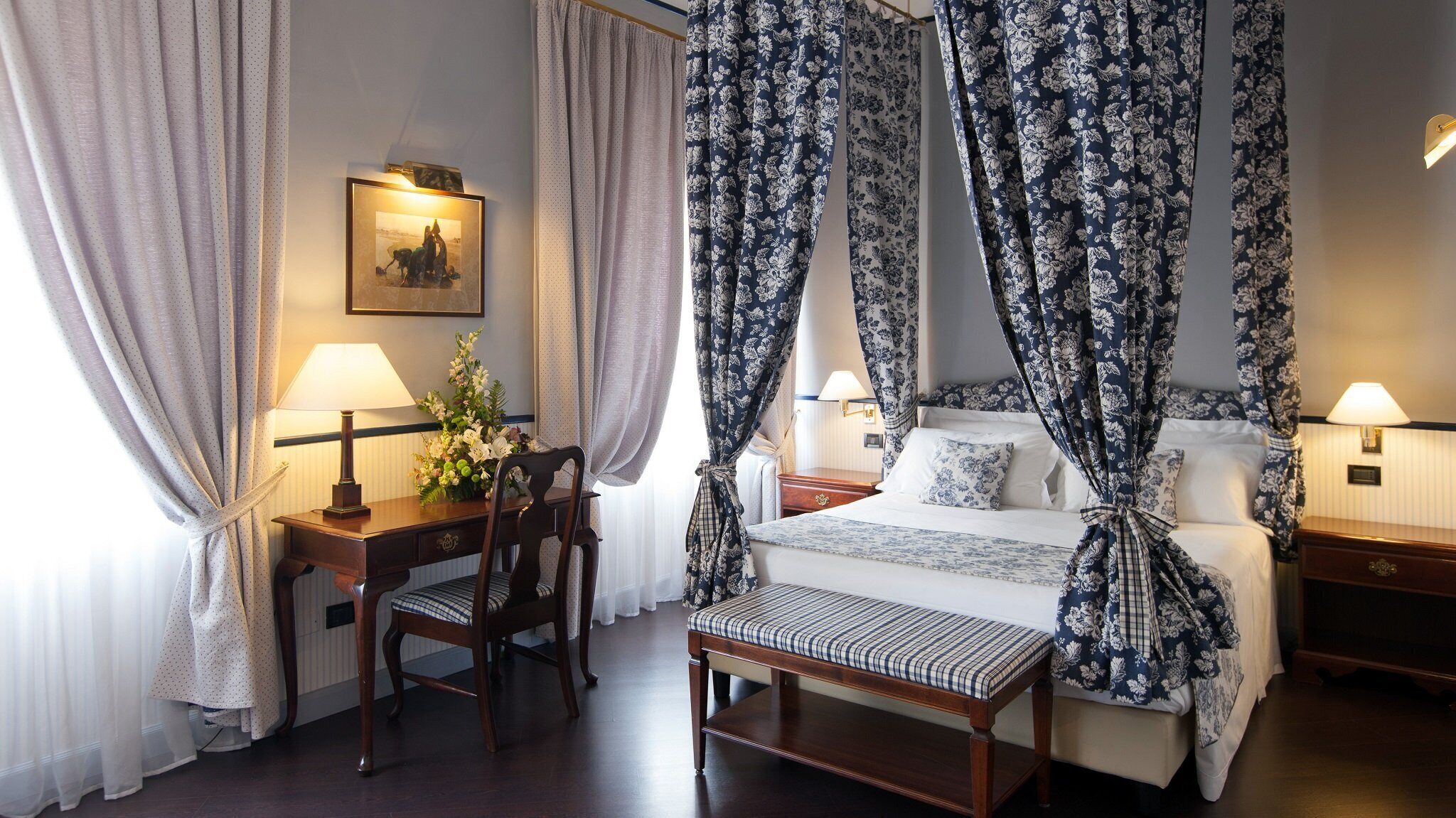 Una habitación de hotel con una cama con dosel, un escritorio con lámpara y una silla.