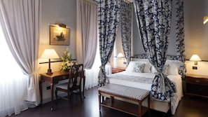 Una habitación de hotel con una cama con dosel, un escritorio con lámpara y una silla.