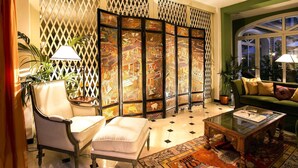 A traditional room with a tatami mat floor, a low wooden table, a cushioned chair, a sofa, and a decorative screen with painted panels. - Hotel Victoria (Turin)