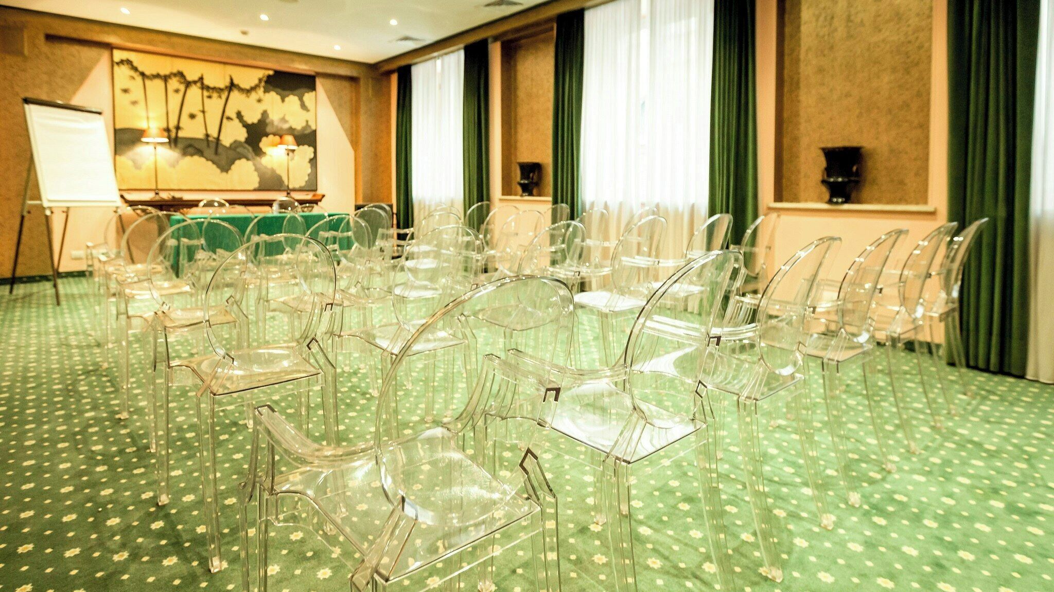 Un salón de conferencias con sillas de plástico transparente dispuestas en filas, una pizarra y un cuadro en la pared.