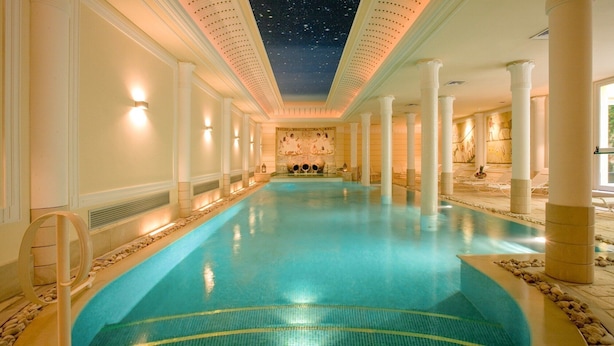 A large indoor swimming pool with a starry ceiling, white columns, and a stone wall with artwork. - Hotel Victoria (Turin)