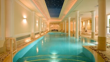 Una amplia piscina cubierta con techo estrellado, columnas blancas y pared de piedra con obras de arte.