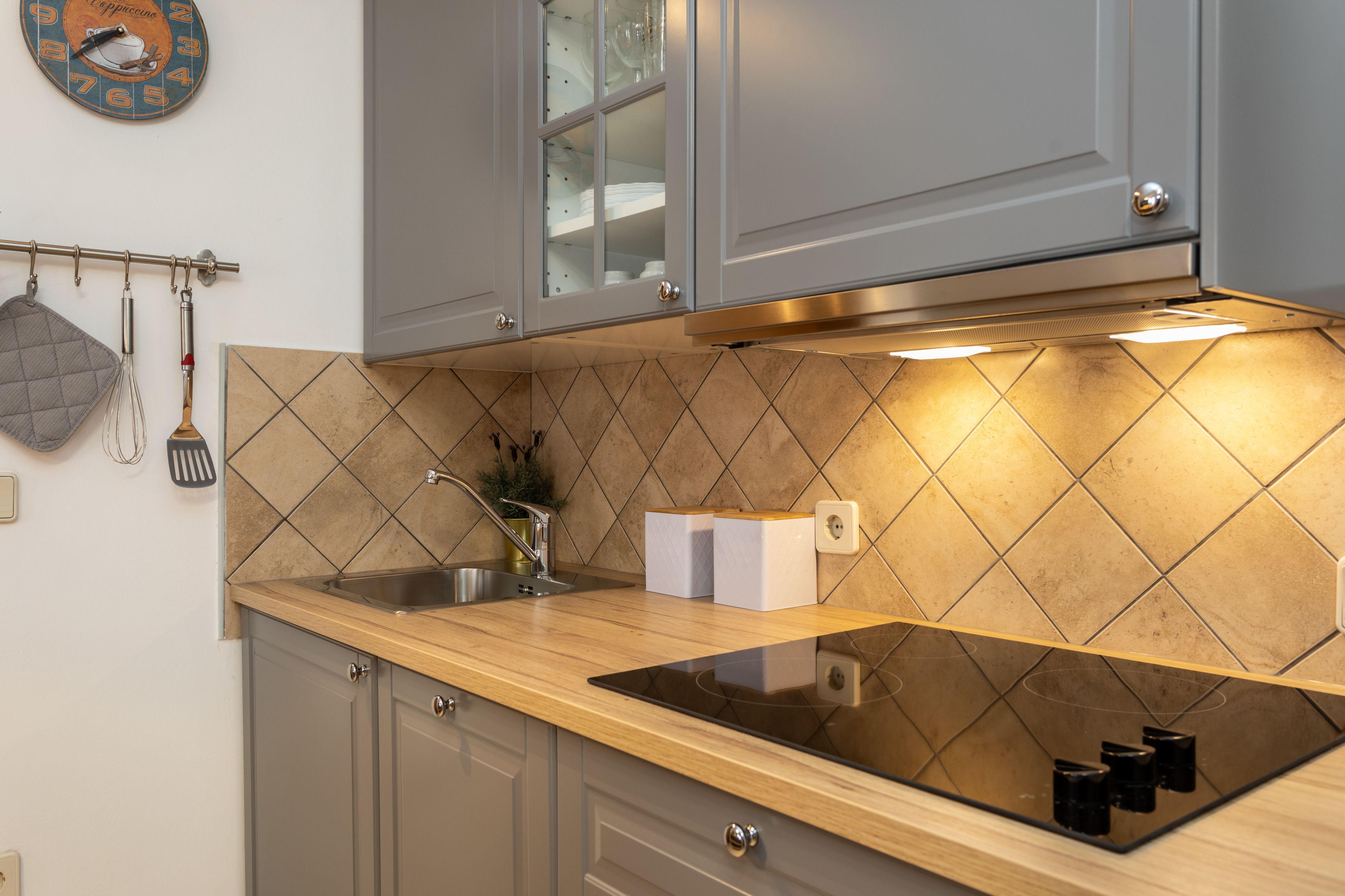 A modern kitchen with grey cabinets, a black induction cooktop, and a tiled backsplash.