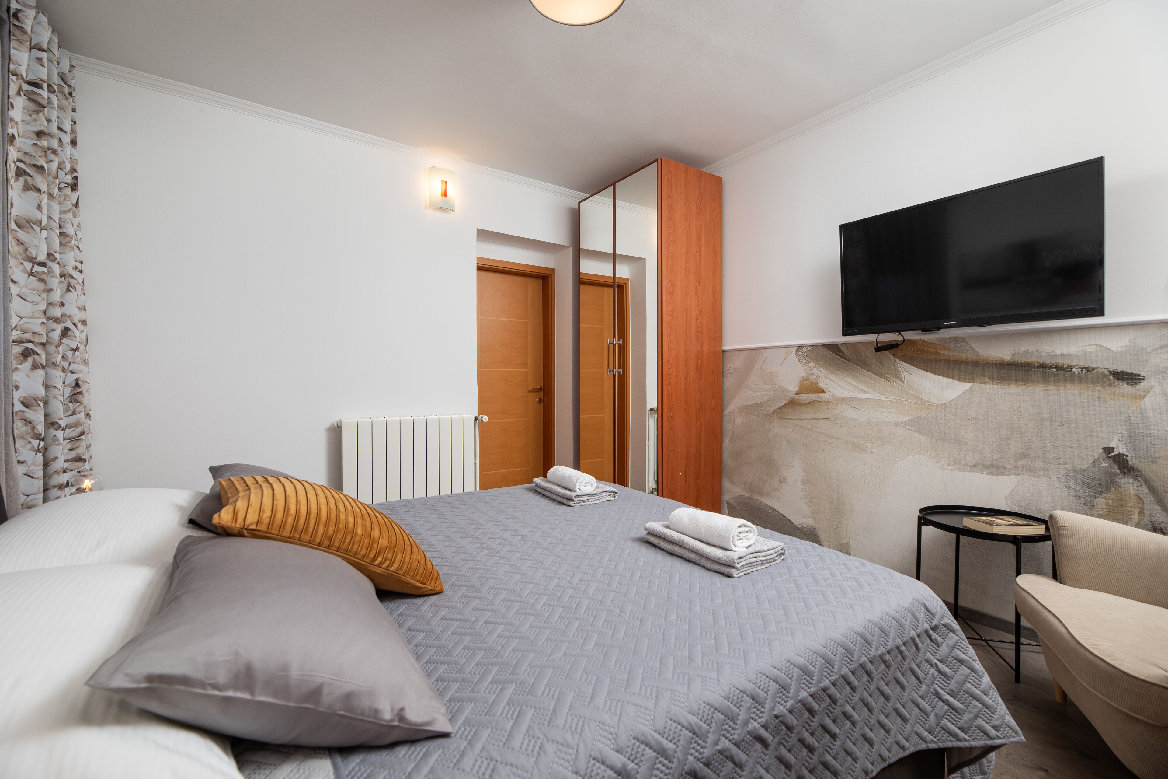 A modern bedroom with a bed, a TV mounted on the wall, a chair, and a small table.