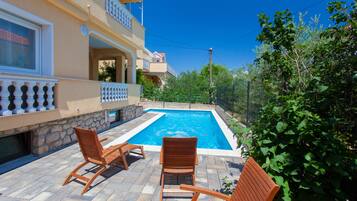 A poolside area with two wooden chairs and a stone wall.