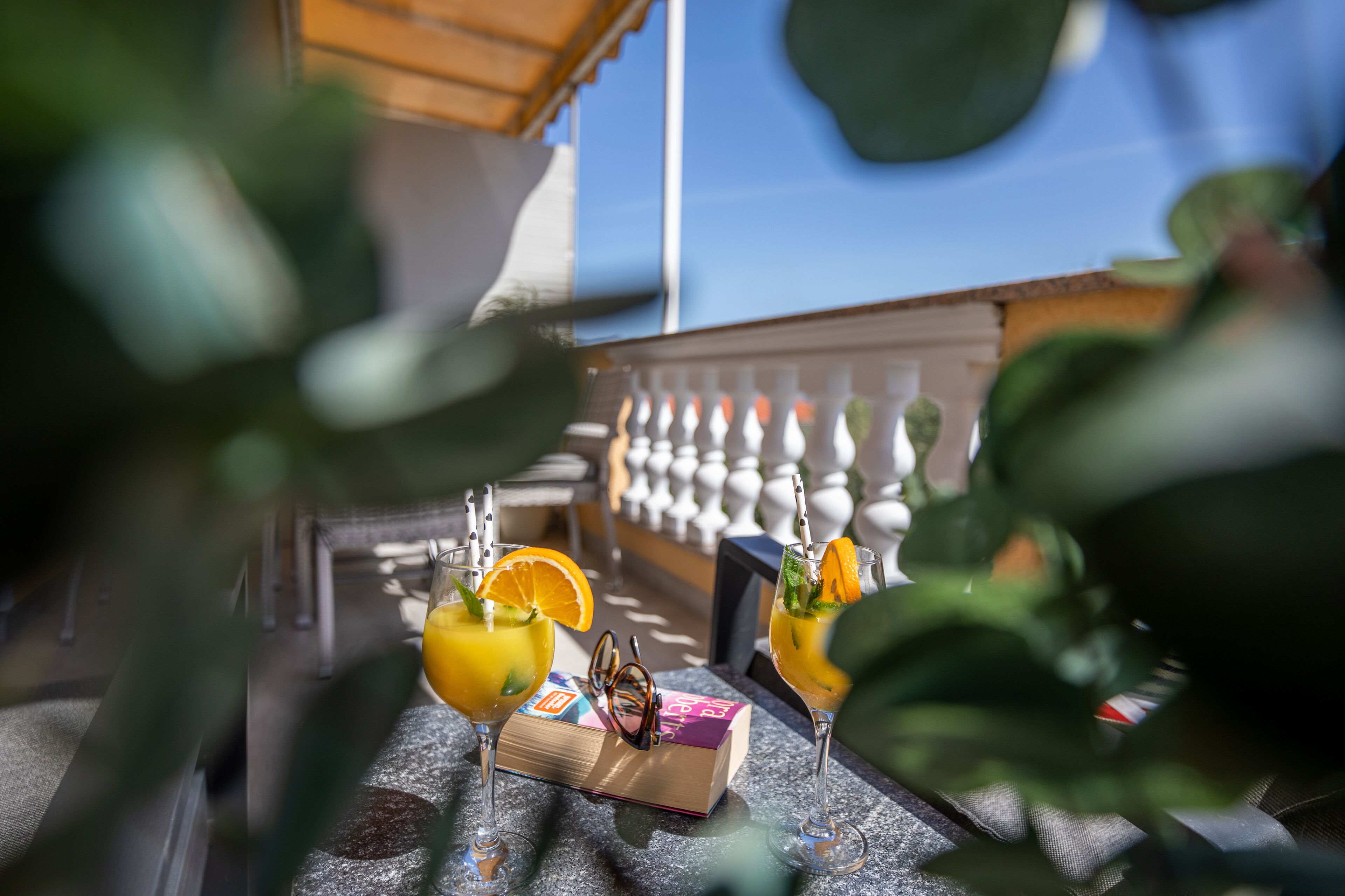 Dos bebidas con adornos de frutas sobre una mesa, un libro y un par de gafas.