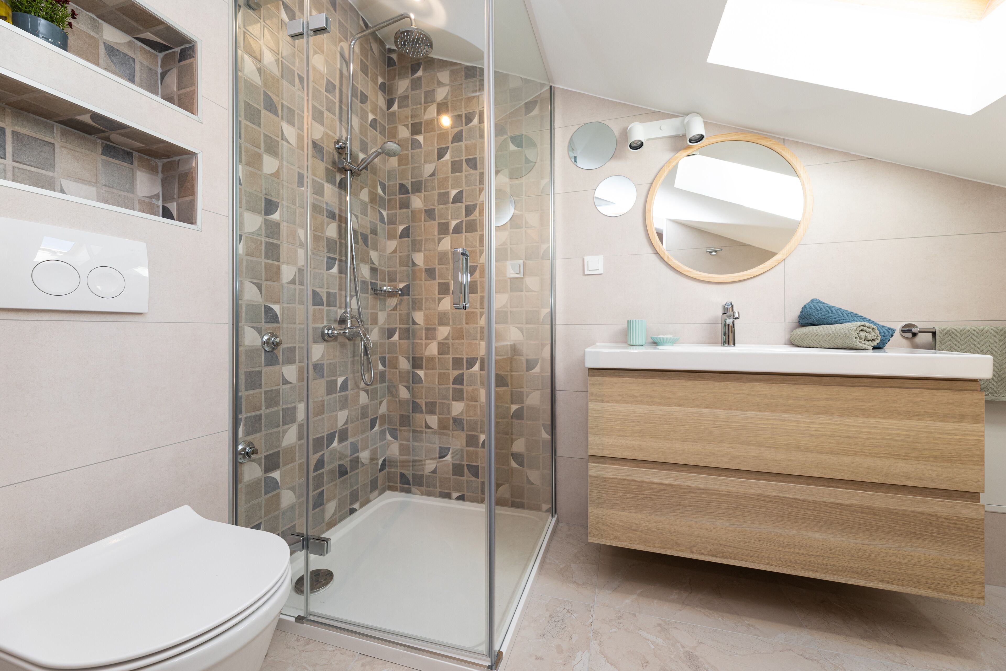 A modern bathroom with a glass-enclosed shower, a white toilet, a wooden vanity, and a skylight.