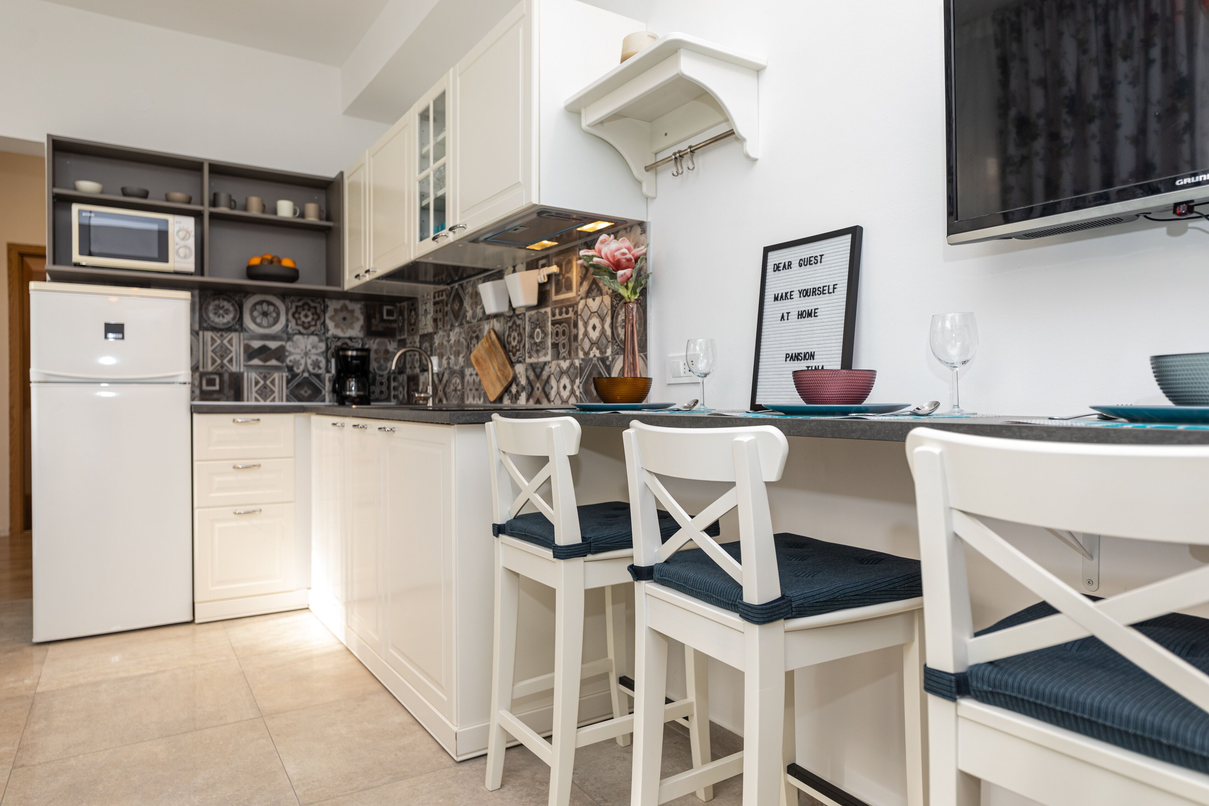 A modern kitchen with white cabinets, a microwave, a refrigerator, and a dining area with white chairs and a table.