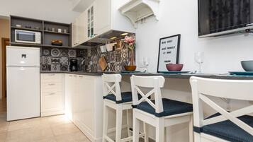 Una cocina moderna con armarios blancos, microondas, refrigerador y una zona de comedor con sillas y mesa blancos.