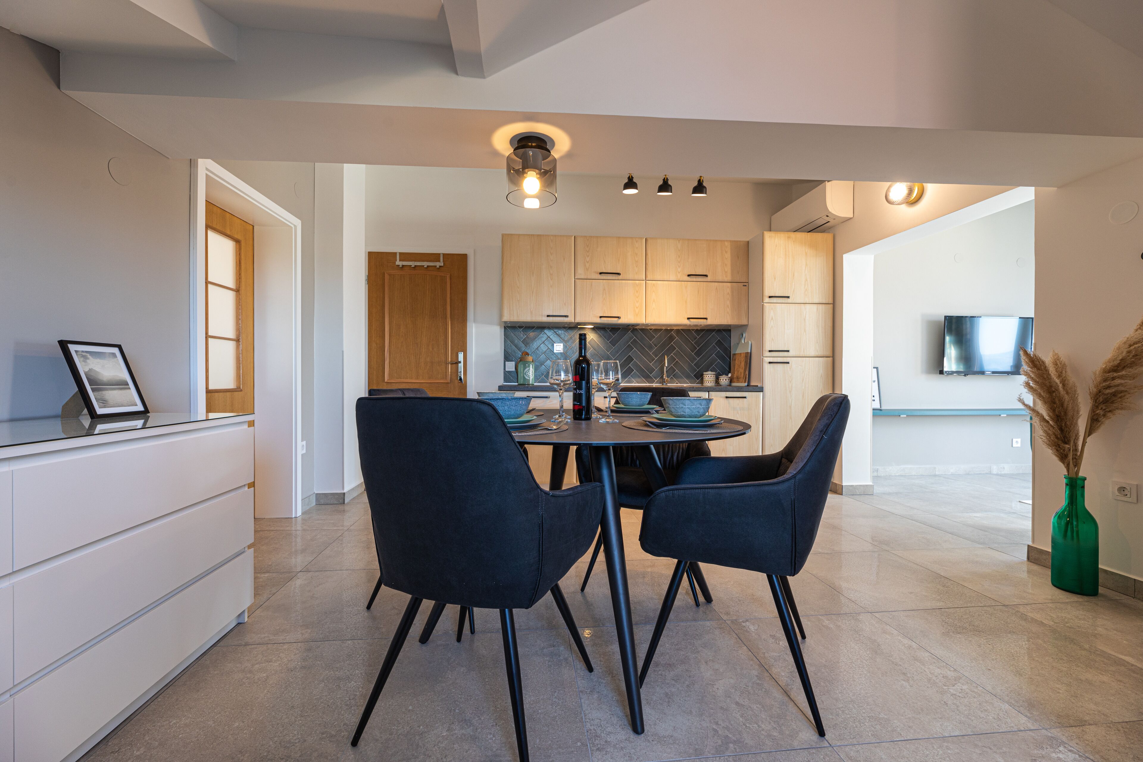 Una cocina moderna con armarios de madera, una mesa de comedor con sillas y un televisor al fondo.